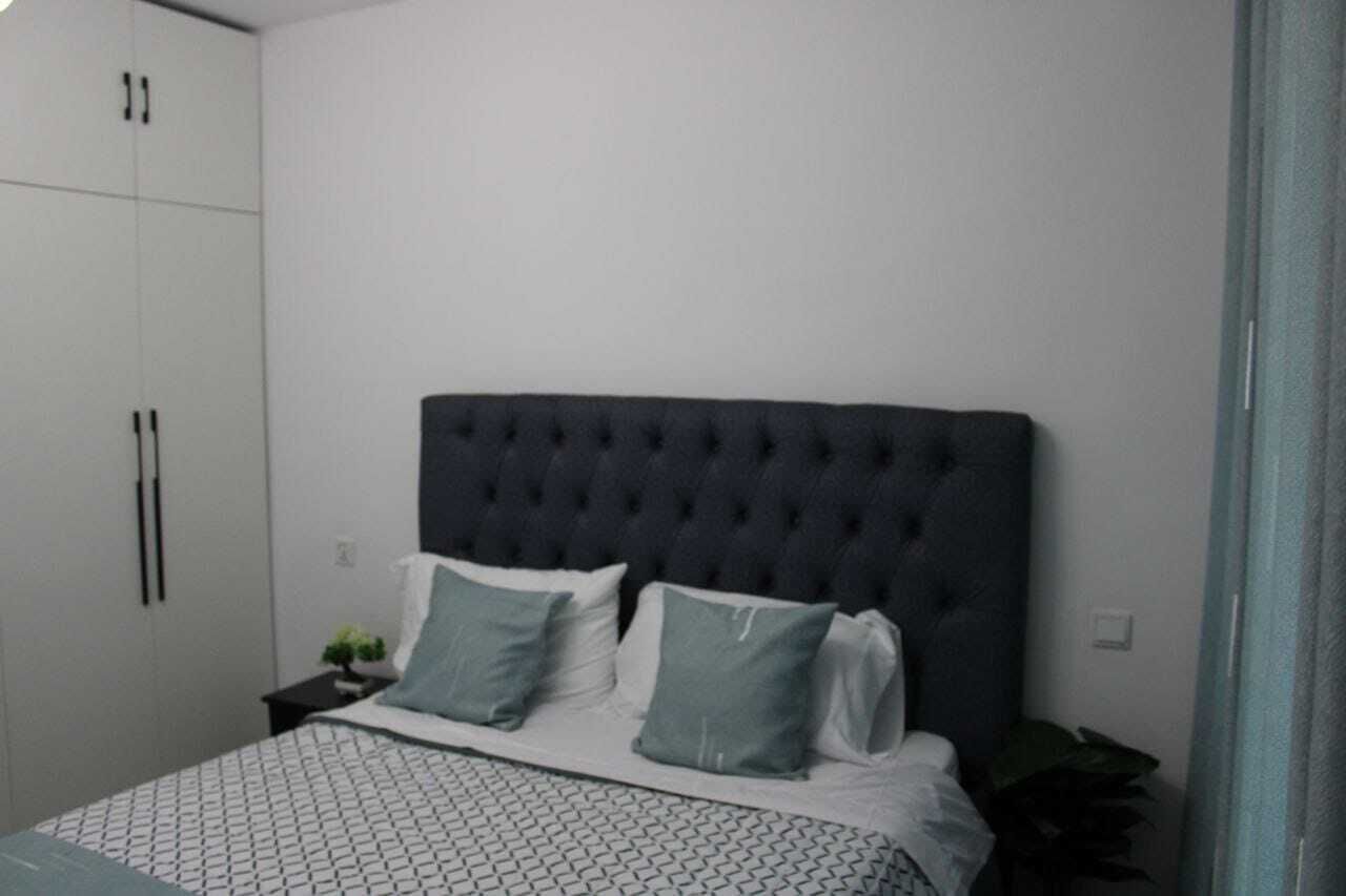 Ein Schlafzimmer mit einer gesteppten Kopfteil, einer gemusterten Tagesdecke und einem Nachttisch mit Pflanze.