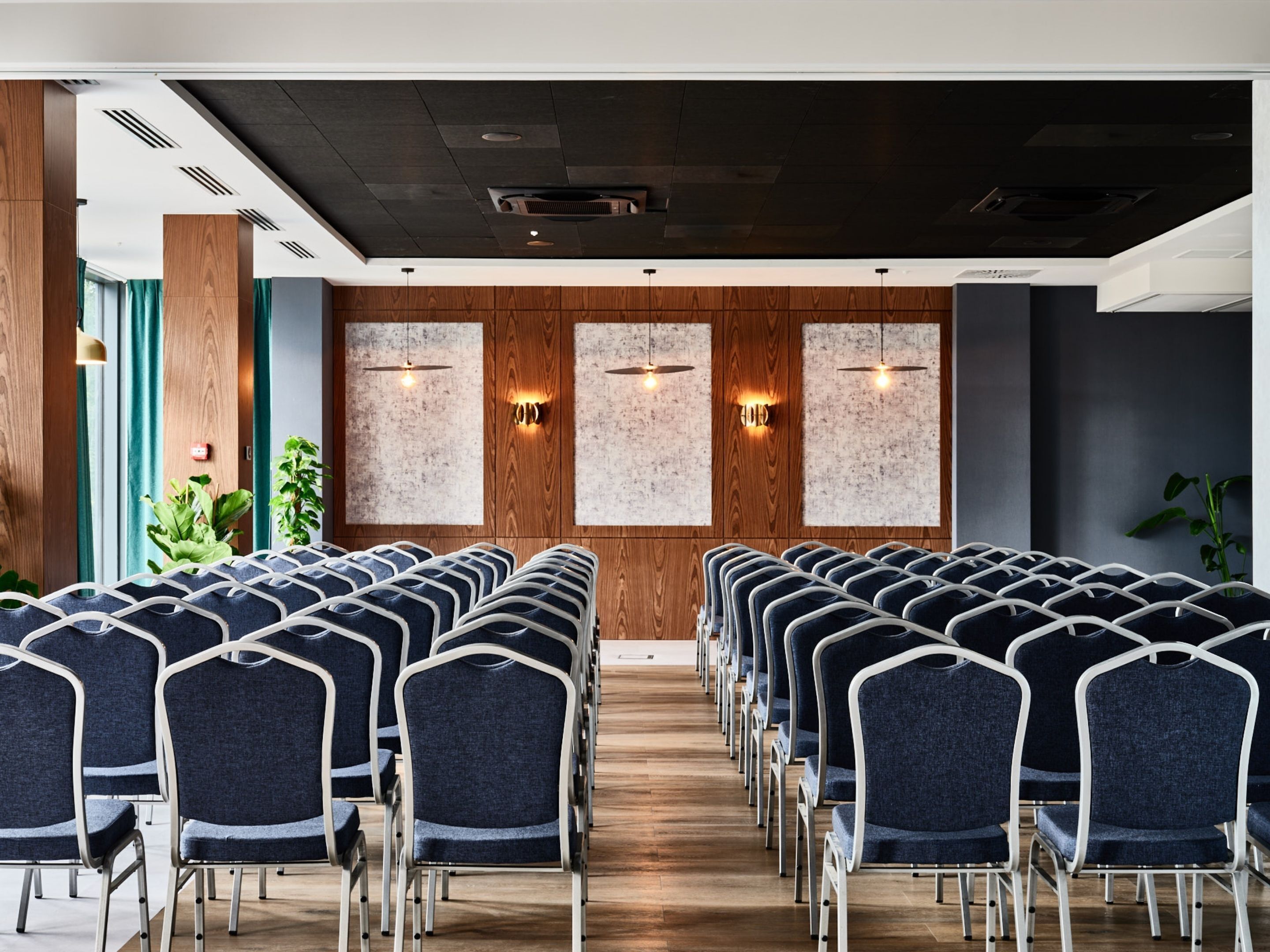 Un salón de conferencias con filas de sillas, paredes de paneles de madera y rejillas en el techo.