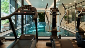 A gym with treadmills and elliptical machines, a glass wall overlooking a pool, and a view of trees outside. - Hotel Bergo Resort & SPA (Szklarska Poreba)
