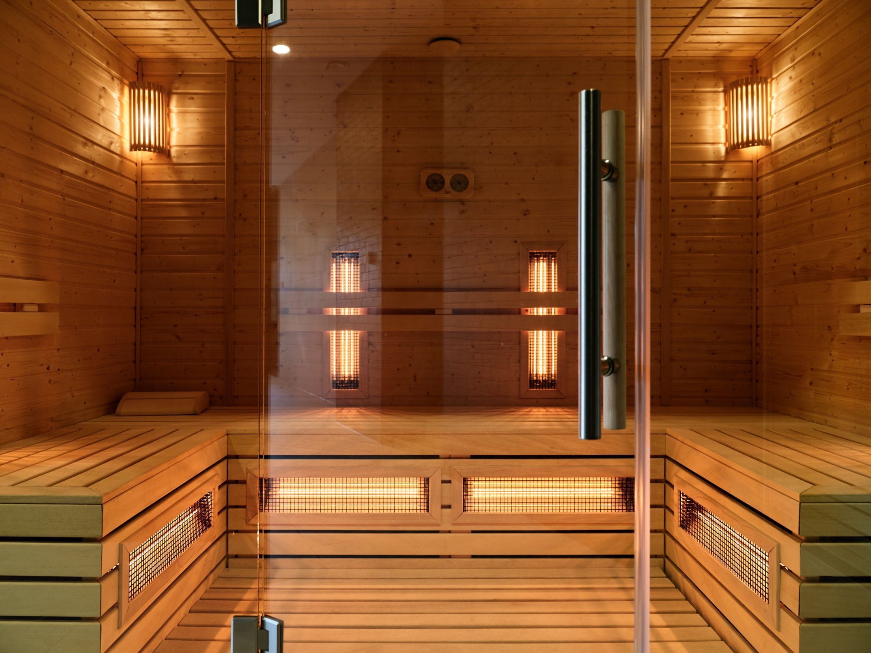 Eine Sauna mit Holzwänden und -boden, Glastüren sowie zwei an der Wand befestigten Leuchten.