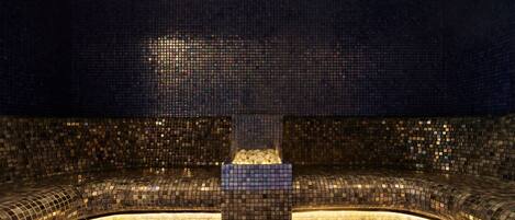 A large, circular pool with mosaic tile walls and a central seating area.
