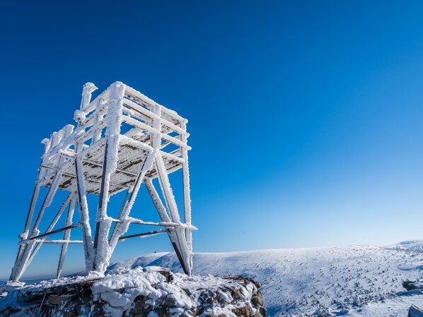 A snow-covered observation tower on a mountain peak with a clear blue sky in the background.