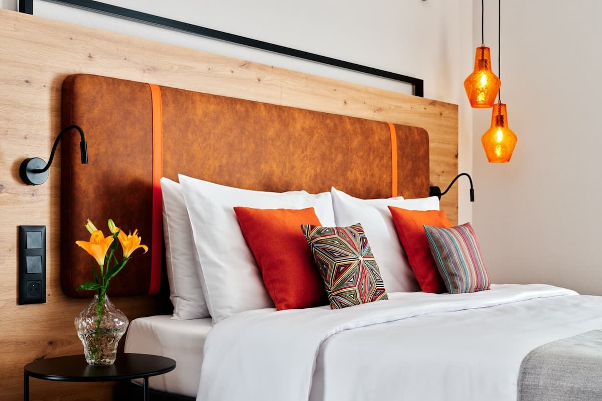 A modern bedroom with a wooden headboard, white bedding, and colorful pillows.