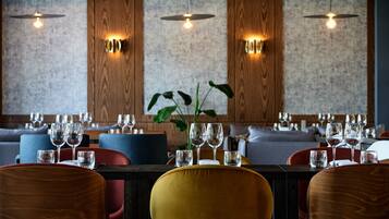 Un restaurante con una mesa larga preparada para comer, paredes de paneles de madera y lámparas colgantes.
