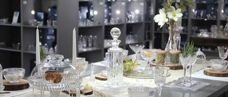 A dining table set with glassware and candles, surrounded by shelves of glassware in the background.