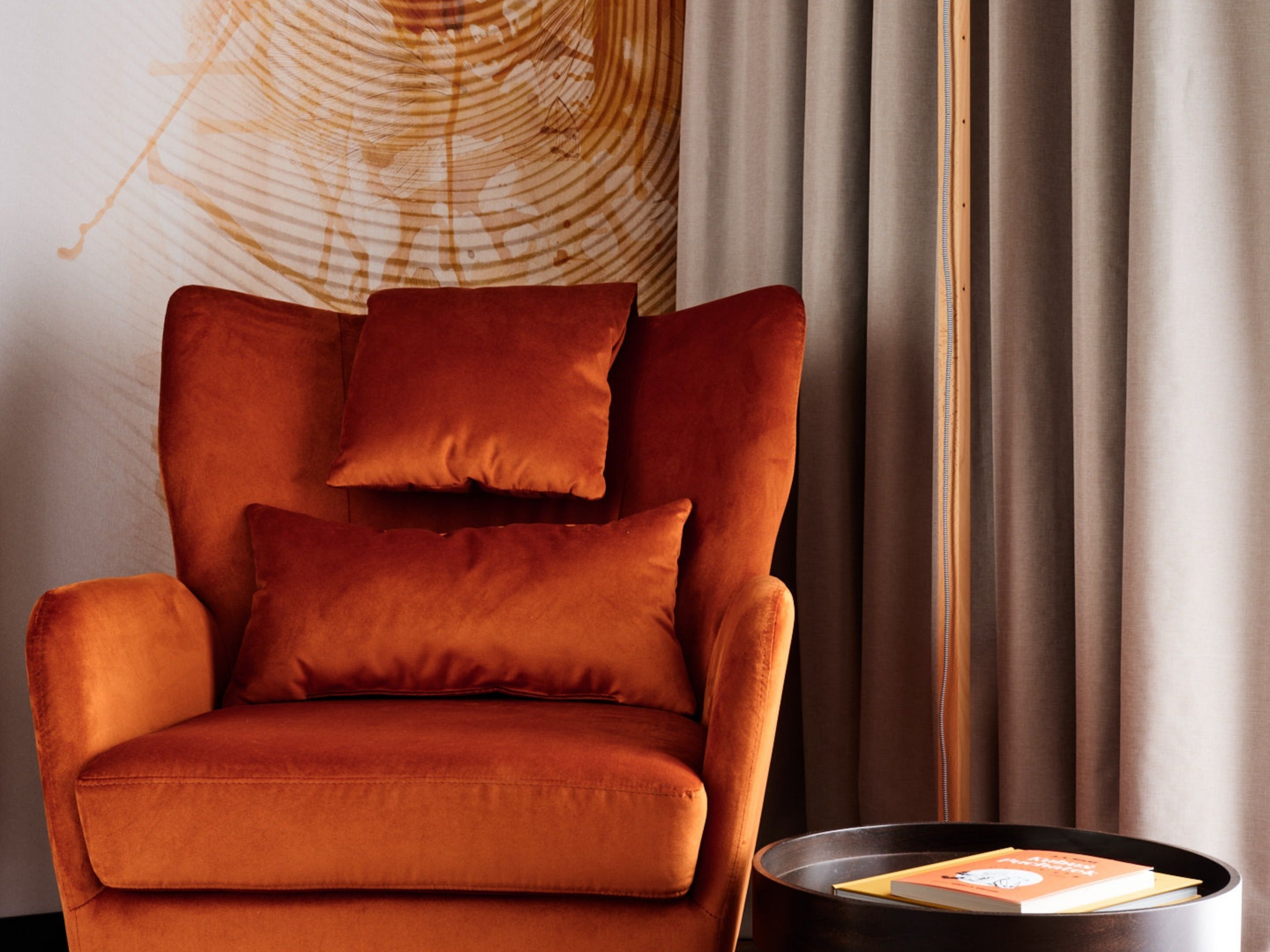 A modern armchair with a cushion, positioned next to a round table with a book.
