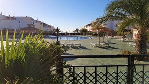 A pool area with lounge chairs and palm trees, surrounded by buildings. - Beach Apartment in Vera Playa for 4 (Vera Playa)