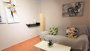 Ein Wohnzimmer mit grauem Sofa, zwei gemusterten Kissen, einem weißen Couchtisch und abstrakter Kunst an den Wänden.