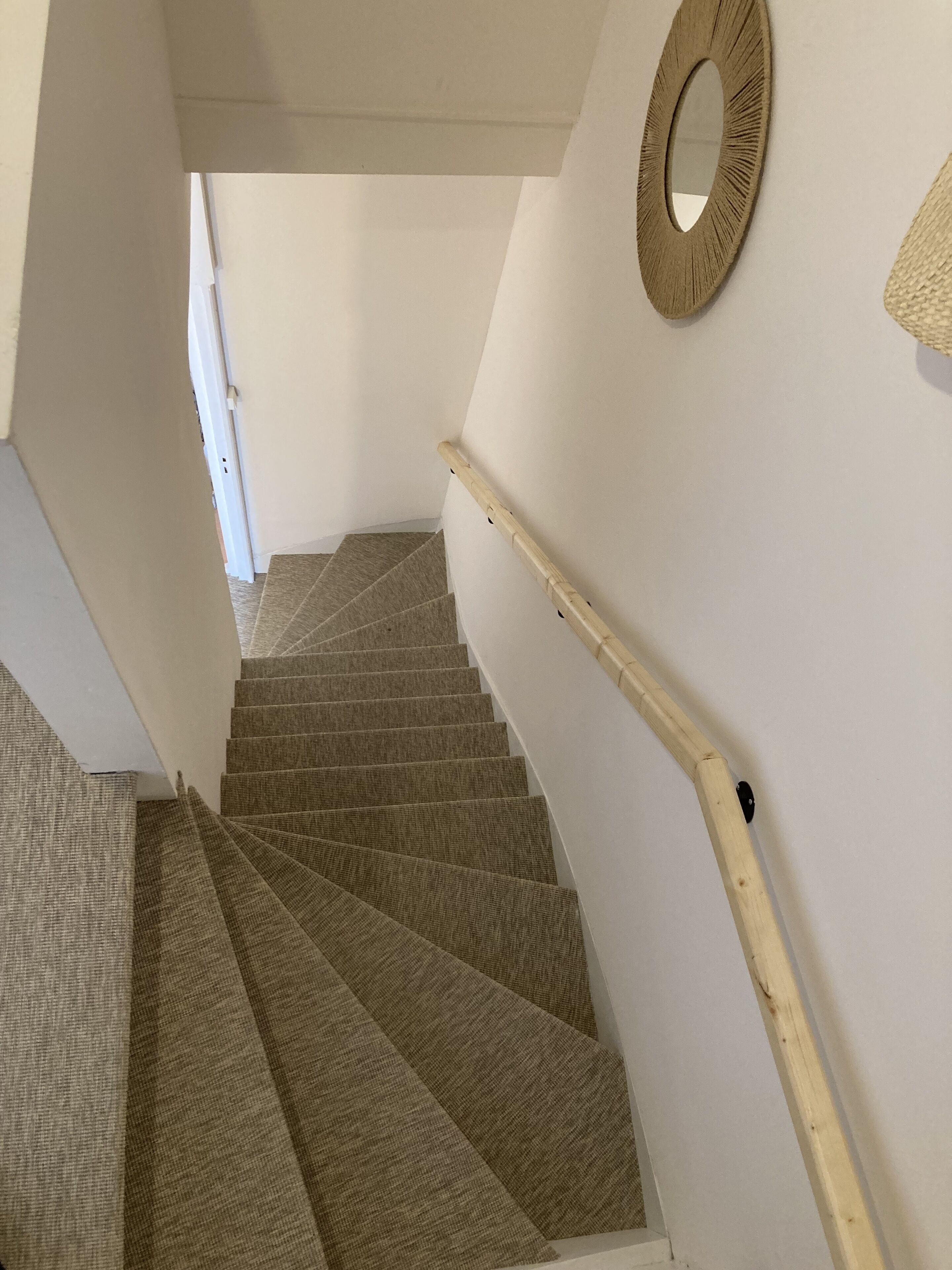 A staircase with a wooden handrail and carpeted steps leading to a landing.