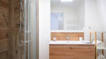 Ein modernes Badezimmer mit Duschkabine aus Glas, einem Holzwaschtisch mit Spiegel und einem Handtuchhalter.