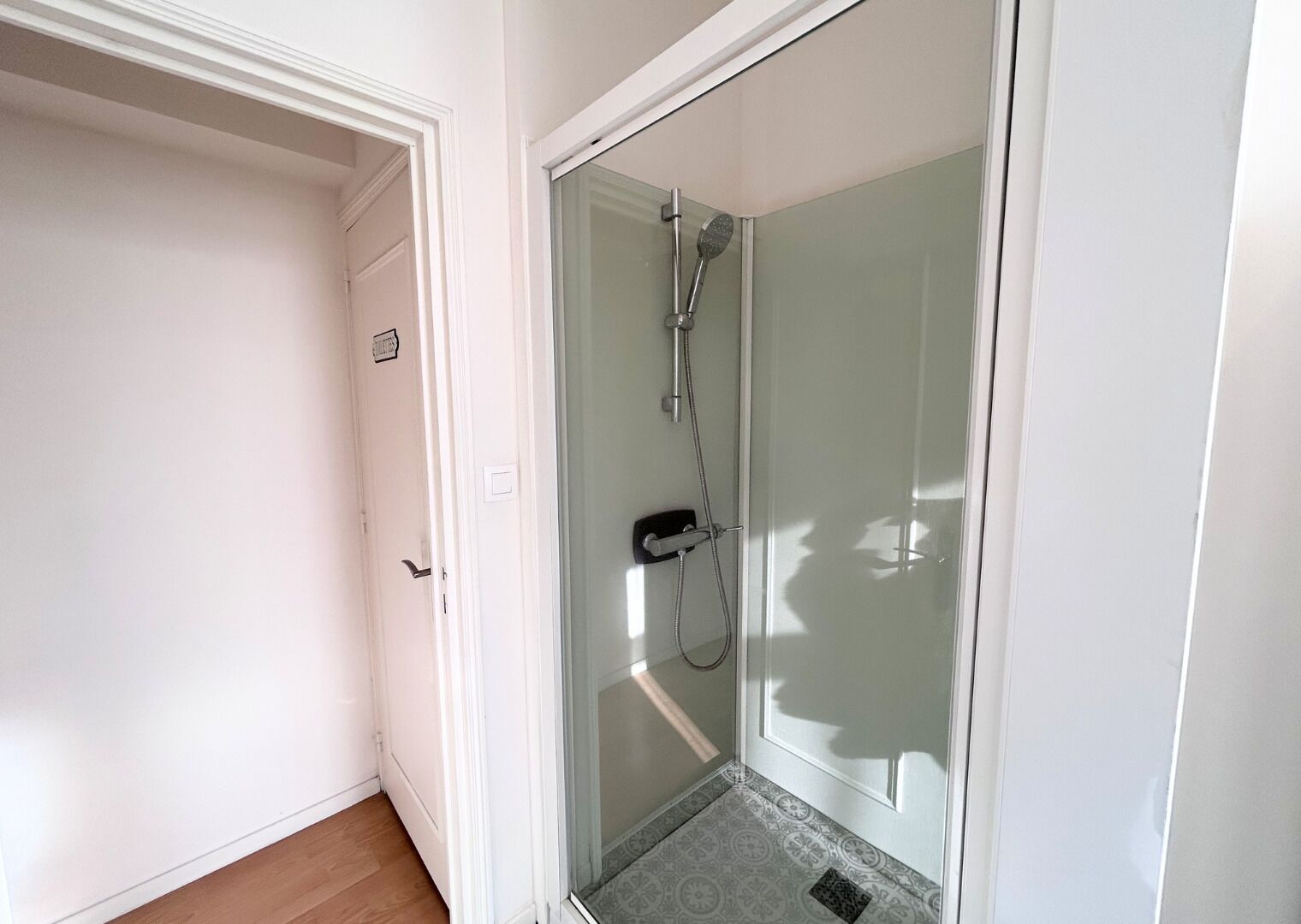 A glass-enclosed shower with a handheld showerhead and a handheld faucet.