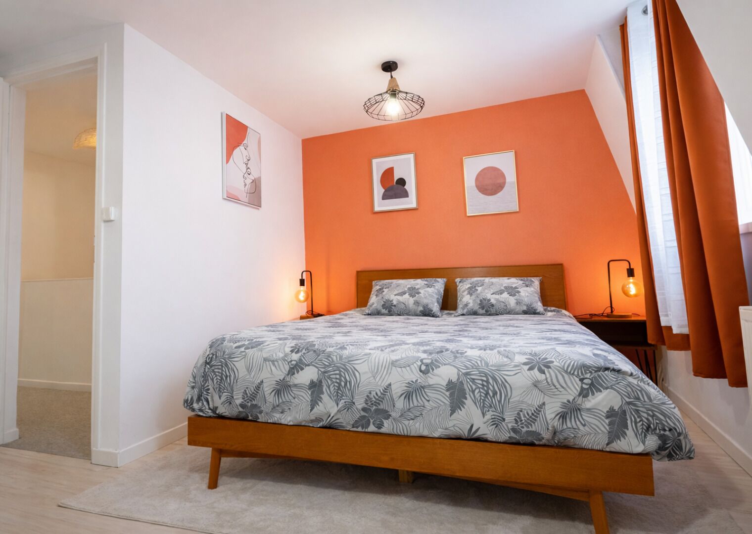 A bedroom with a bed, two bedside lamps, a ceiling light, and two framed pictures on the wall.