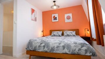 A bedroom with a bed, two bedside lamps, a ceiling light, and two framed pictures on the wall.