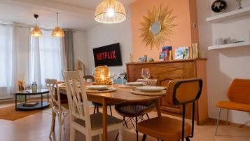A dining area with a table set for four, chairs, pendant lights, a wall-mounted TV, and a decorative mirror.