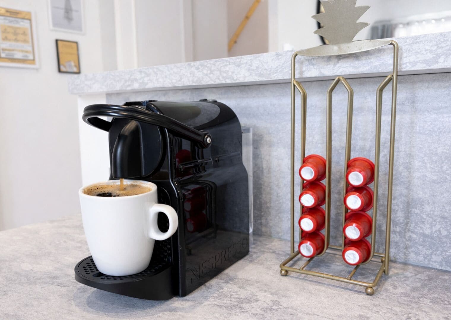 A coffee maker with a cup of coffee, a metal cup holder with red cups, and a marble countertop.