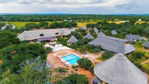 A resort with thatched-roof huts, a swimming pool, and lush greenery.