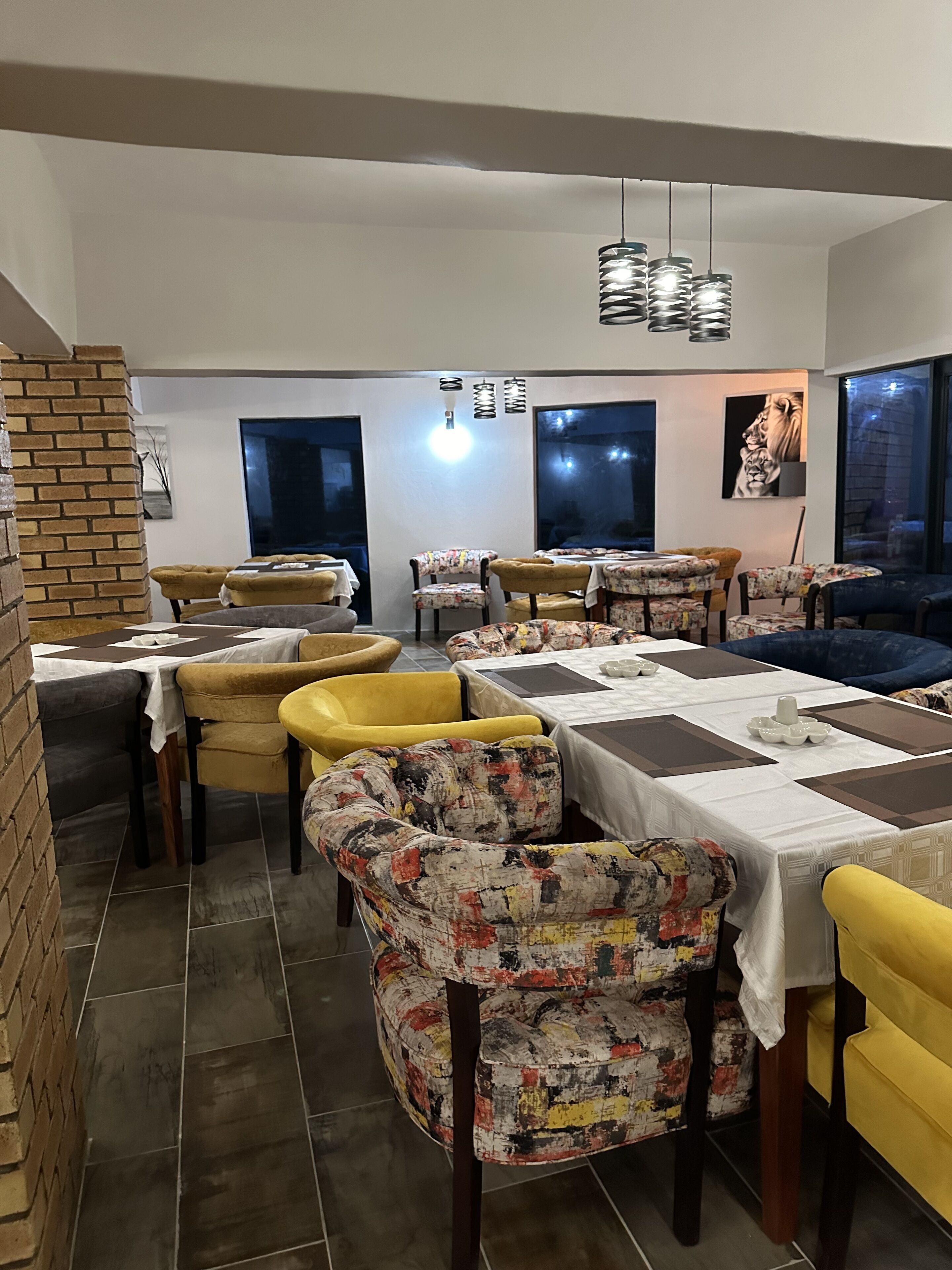 Un restaurante con varias mesas y sillas, un muro de ladrillo y un ventanal grande.