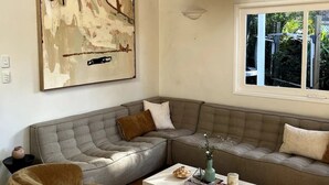 Ett modernt vardagsrum med en stor, abstrakt tavla, en grå hörnsoffa, en beige fåtölj och en vit hänglampa.