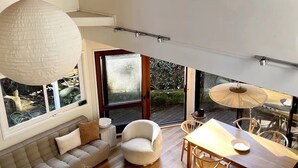 En modern inredning med en soffa, en rund fåtölj, ett matbord och stora fönster som ger utsikt över omgivningen.