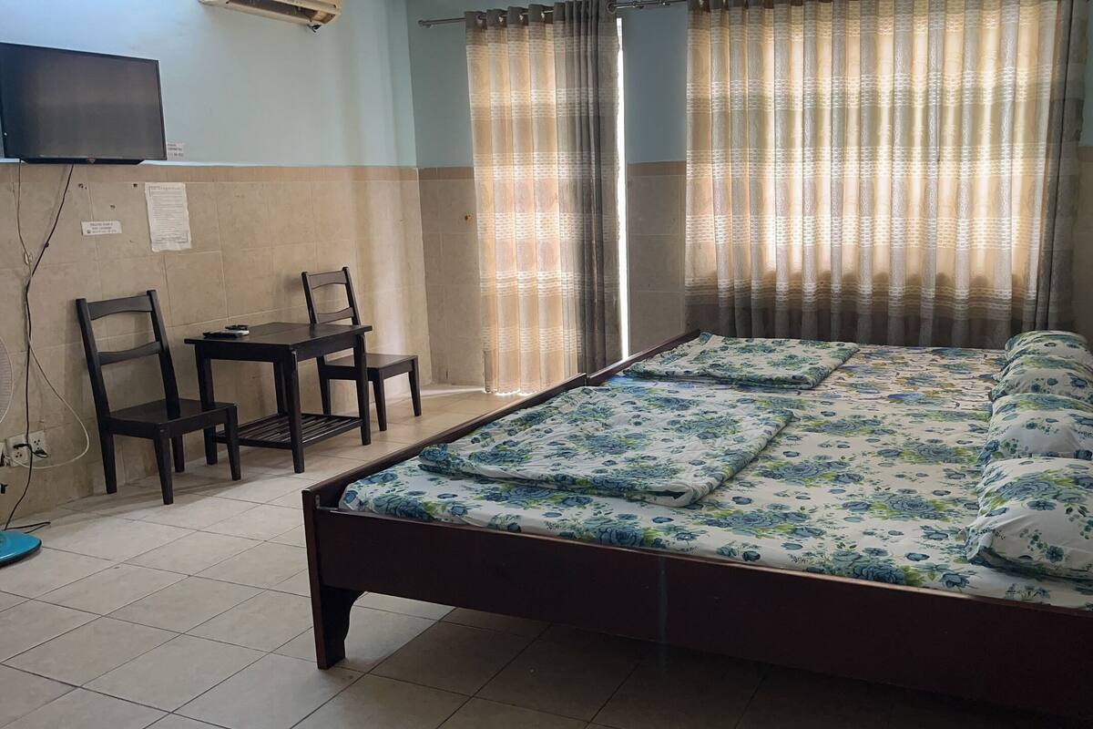 A bedroom with a bed, a desk, two chairs, a TV, and curtains.