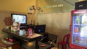 A hotel reception area with a computer, a refrigerator stocked with beverages, a decorative cat figurine, and a wall-mounted sign listing destinations like Paris and London. - Thanh Nam Hotel - by Bay Luxury (Ho Chi Minh City)