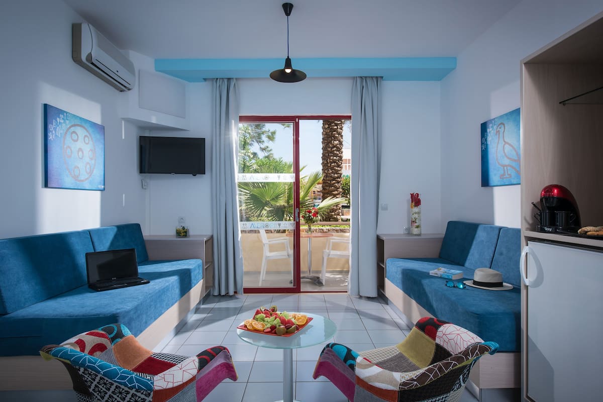 A modern living room with two blue sofas, a glass coffee table with fruit, and a sliding glass door to a balcony.