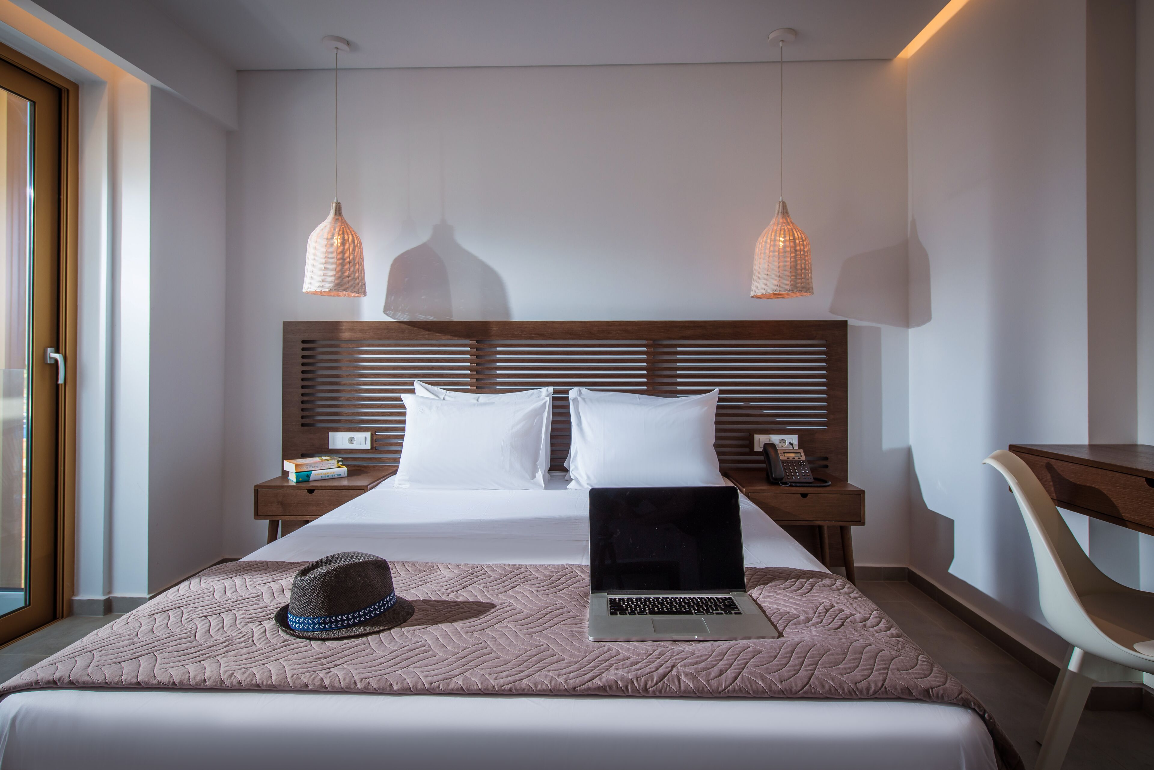 A hotel room with a bed, a laptop, a hat, and two pendant lights.