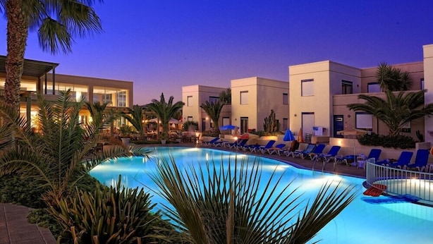 A swimming pool with lounge chairs, palm trees, and modern buildings at dusk. - Meropi Hotel (Hersonissos)