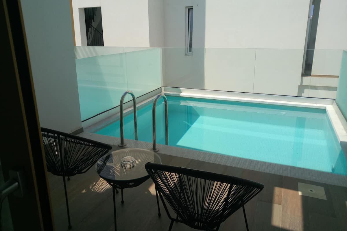 A pool area with a glass barrier, two chairs, and a small table.
