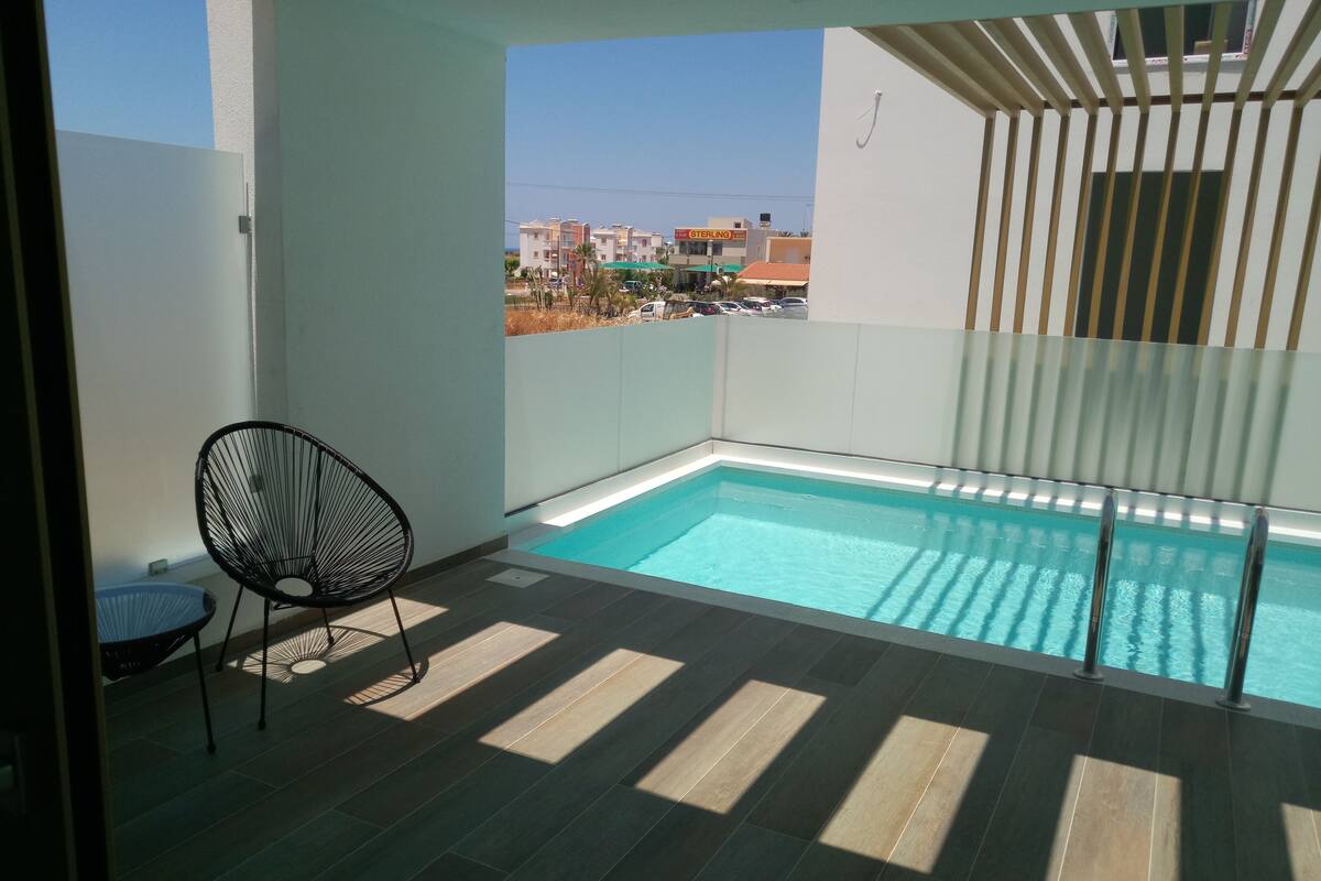 A small balcony with a pool, a chair, and a view of the city.