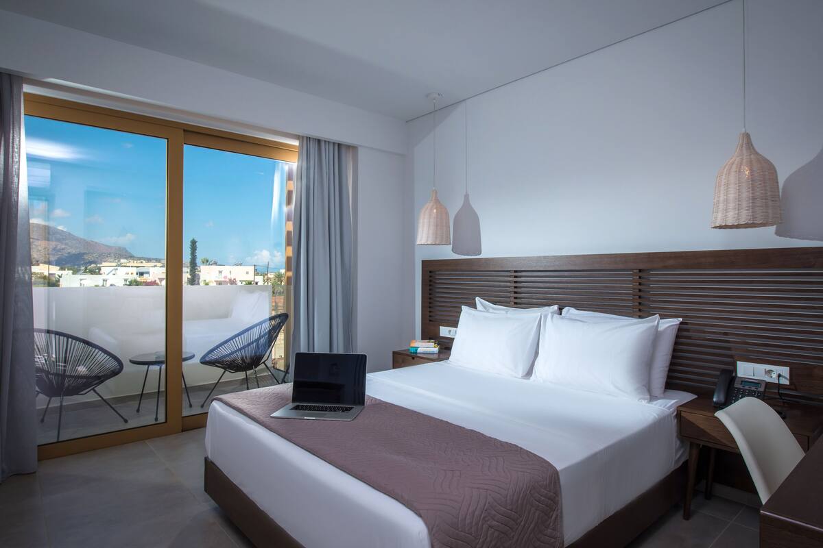 A hotel room with a bed, a laptop, a desk, and a chair.