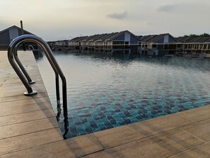 En swimmingpool med en metalstige, træterrasse og moderne bygninger i baggrunden.