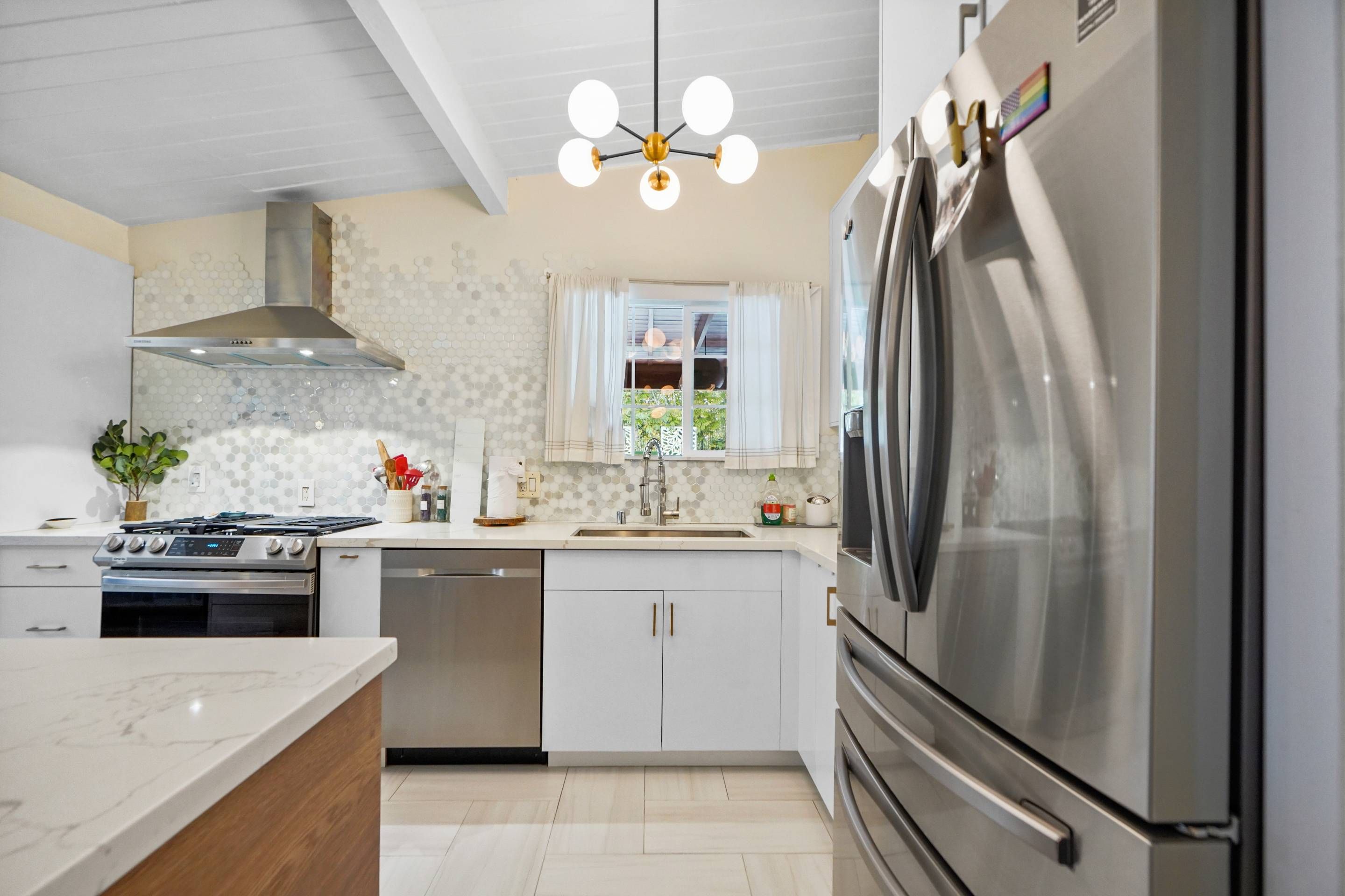 A modern kitchen with a stainless steel refrigerator, a built-in oven, a gas stove, and a pendant light.