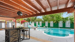 Ein Außenpoolbereich mit einer Holzpergola, einer Bar und Lounge-Möbeln.
