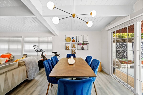 A dining area with a wooden table and blue chairs, a ceiling light fixture, and a view through a glass door to an outdoor patio.
