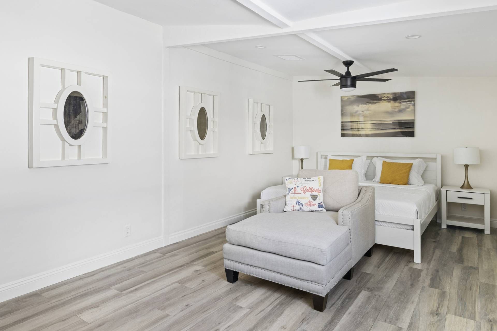 A modern bedroom with a large bed, a grey armchair, and a ceiling fan.