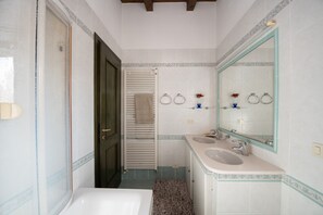 Une salle de bain avec une baignoire, deux lavabos, un porte-serviettes et un miroir.