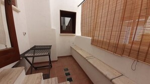 A small, enclosed patio area with a metal table and bench, a window with a mirror, and a wall with a bamboo blind. - 2 Bedroom Apartment in Specchiolla (Specchiolla)