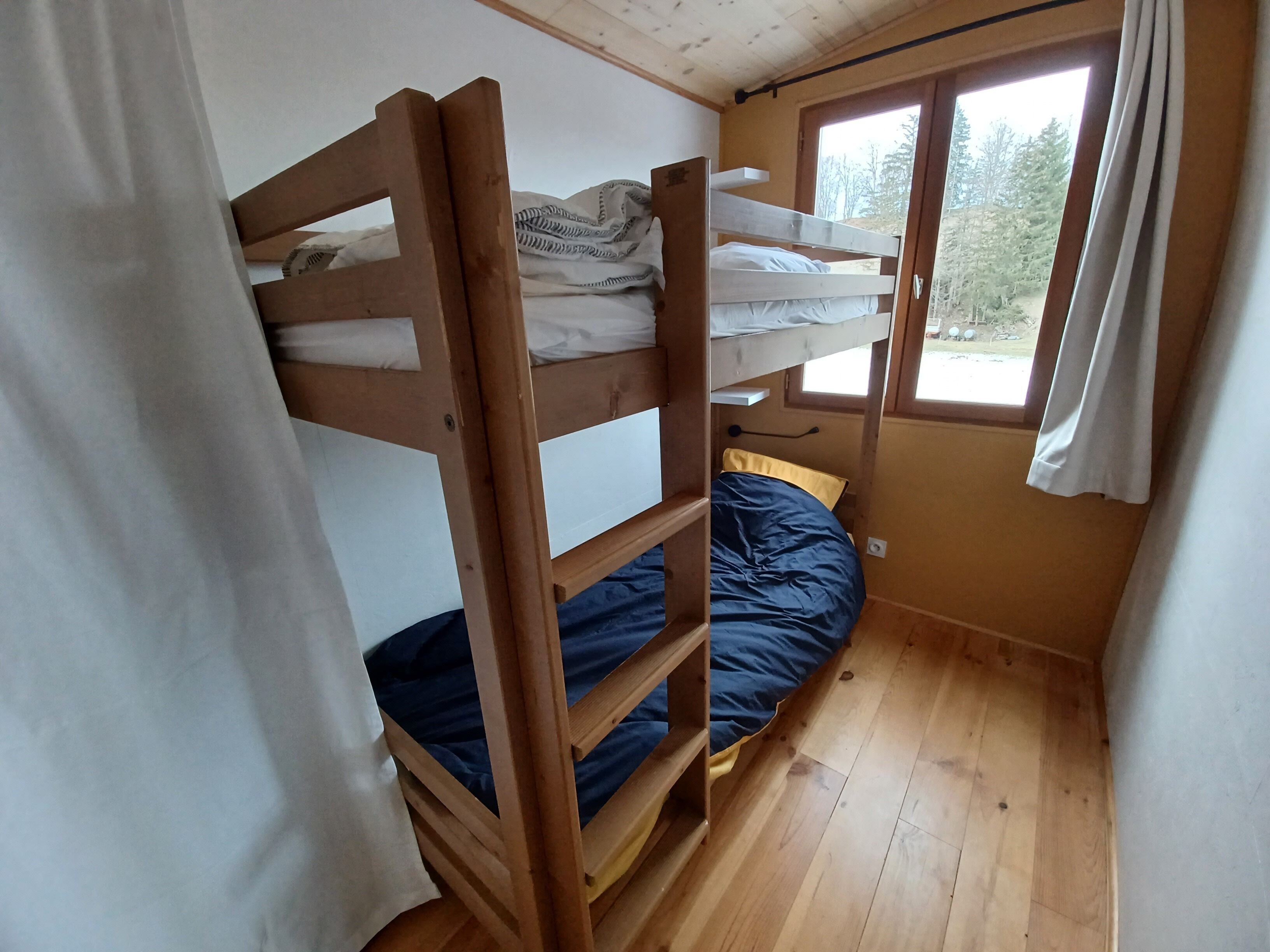 A bunk bed room with a window, wooden flooring, and a curtain.