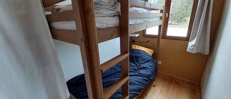 A bunk bed room with a window, wooden flooring, and a curtain.
