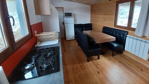 A compact kitchen with a stove, microwave, and refrigerator. There is a dining area with a table and black chairs. - Tiny House in Méaudre in the heart of nature (Vercors plateau) (Autrans-Méaudre en Vercors)