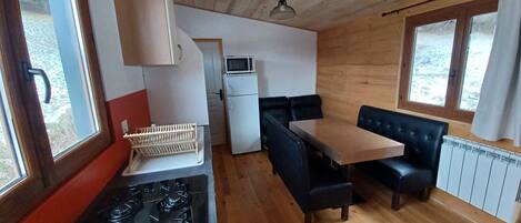 Cocina compacta con estufa, microondas y refrigerador. Cuenta con un comedor con mesa y sillas negras.