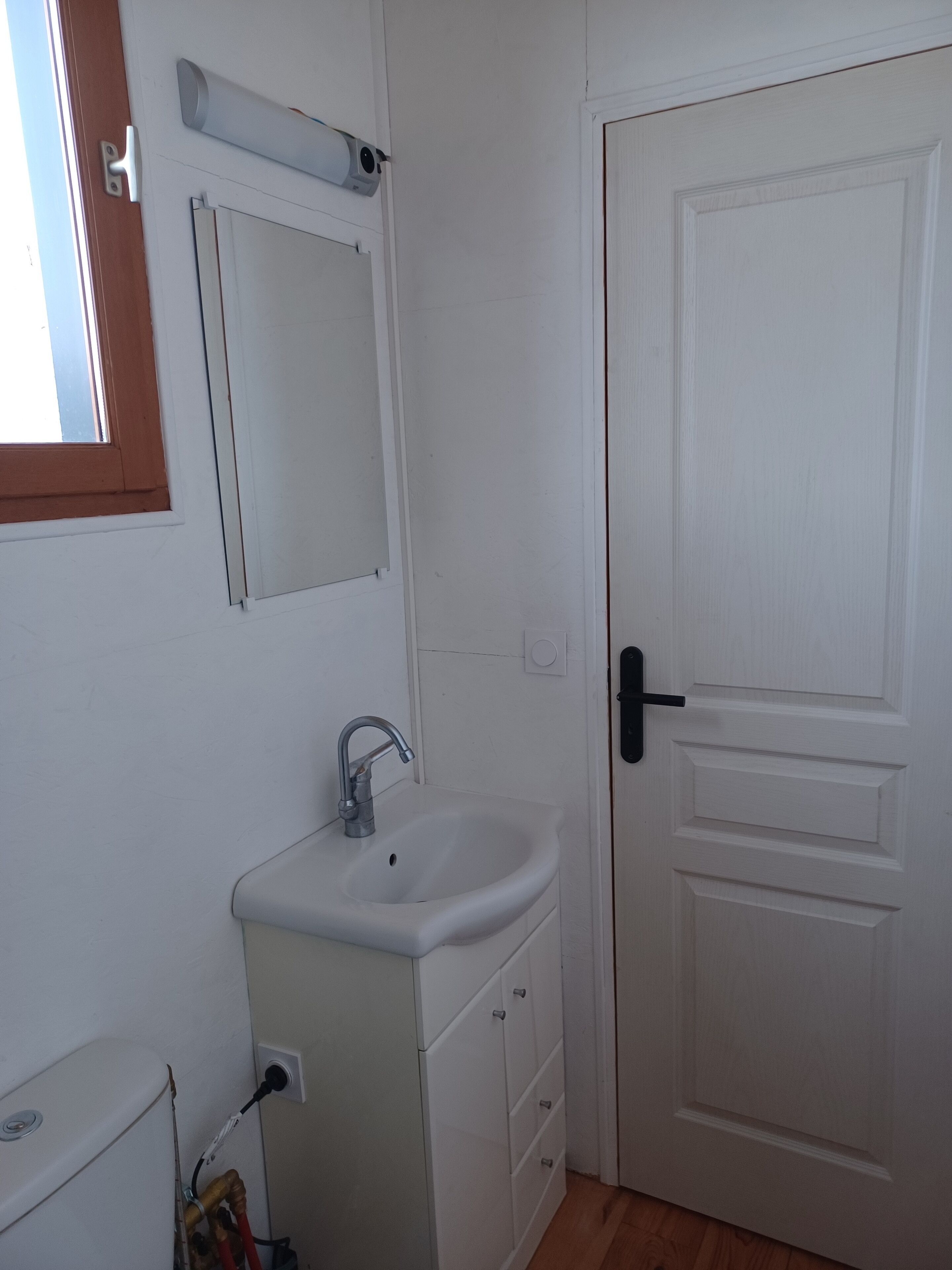 Un baño con lavamanos, espejo y puerta blancos.