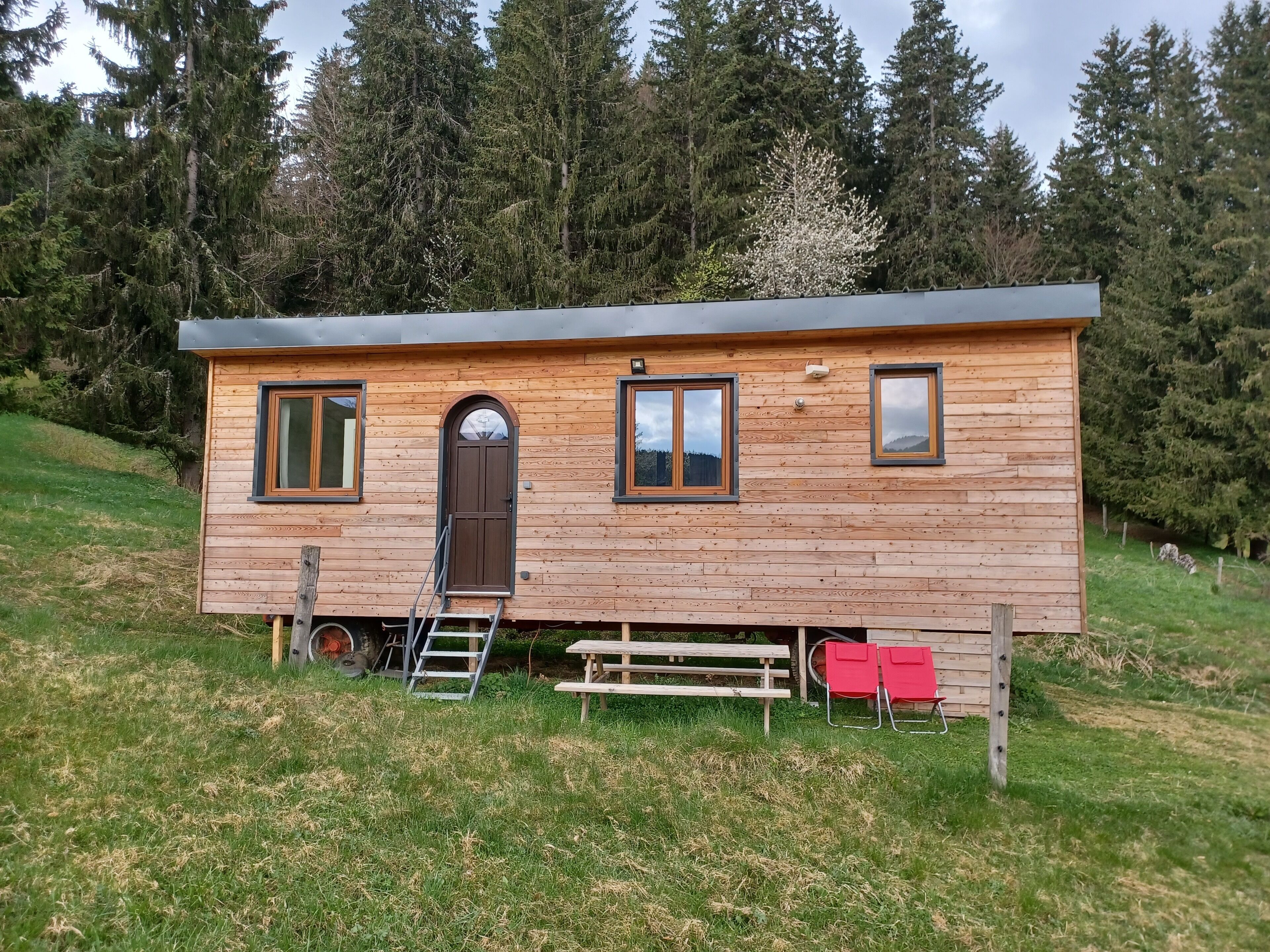 A wooden cabin with a front door, two windows, a small porch, and a ladder.