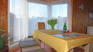 A dining area with a table covered by a yellow tablecloth, a vase with flowers, a bottle, and some magazines.