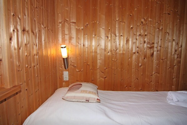 A wooden paneled wall with a wall-mounted light fixture and a bed with a pillow.