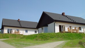 A two-story house with a sloped roof, a visible chimney, and a paved pathway leading to the entrance.