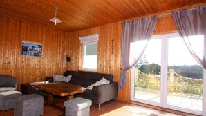 A wooden-paneled room with a sofa, two armchairs, a coffee table, and a large window with curtains.