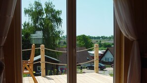 A view from a window with curtains, overlooking a wooden deck with a rope swing, a house, and a car in the background.