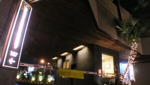 Una entrada nocturna con un cartel indicativo, un acceso con portón y una palmera.